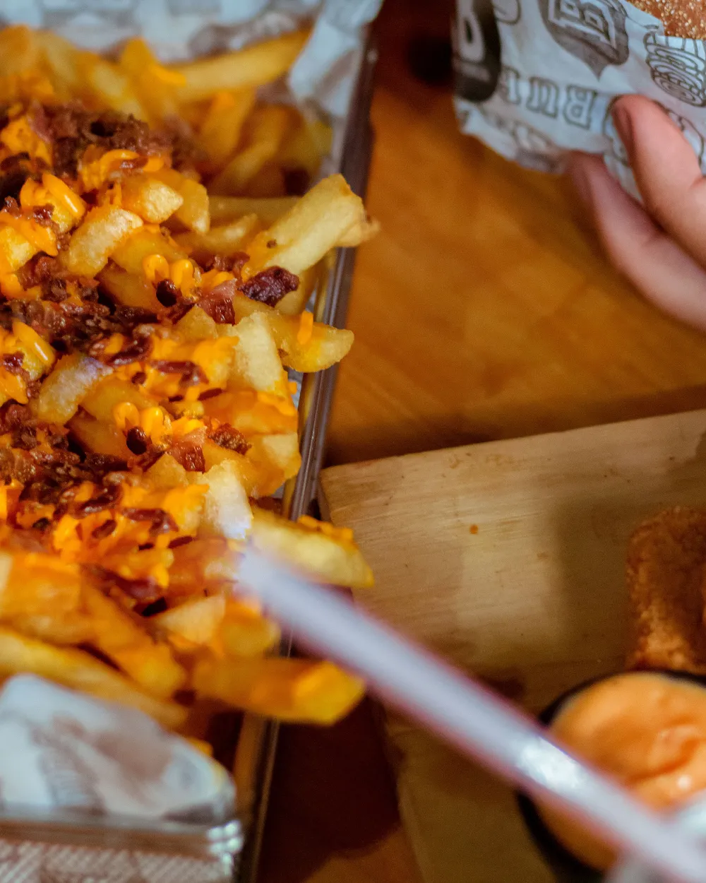 Papas con queso y tocino junto a una hamburguesa.